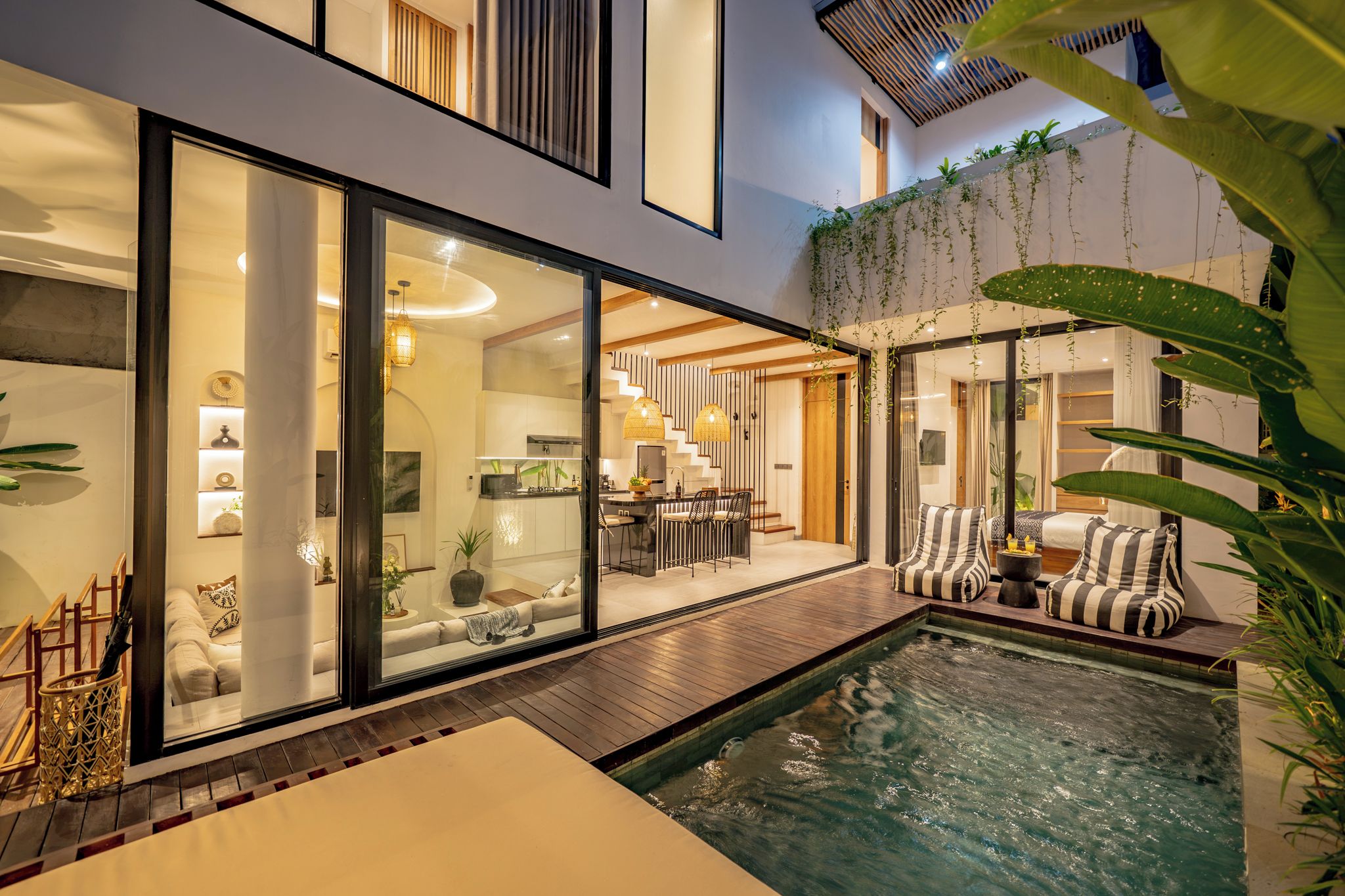 A modern outdoor living area with a pool, a dining area, and a kitchen visible through glass doors.