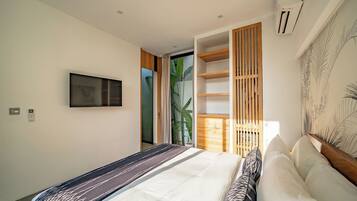 Un dormitorio moderno con cama, televisor en la pared y ventana con vista a follaje.