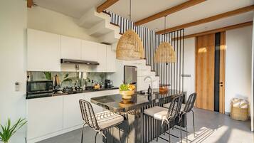 Een moderne keuken met een centraal eiland, roestvrijstalen apparatuur en een eethoek met rieten stoelen.