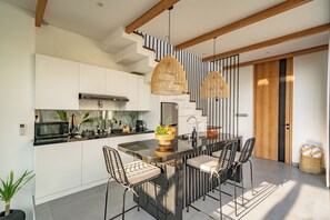A modern kitchen with a central island, stainless steel appliances, and a dining area with wicker chairs. - Villa Scorpia 1 Bingin (Pecatu)