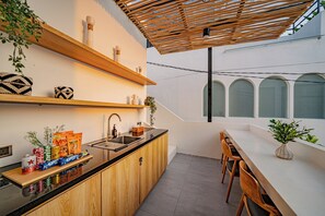 Een moderne keuken met houten kastjes, een spoelbak en een aanrecht met lekkernijen. Er is een eethoek met een tafel en stoelen.