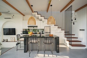 A modern kitchen with a central island, black and white striped walls, and a staircase with wooden steps. - Villa Scorpia 1 Bingin (Pecatu)