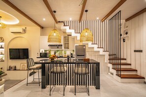 Eine moderne Küche mit einer zentralen Kochinsel, schwarzen Barhocker und einer Treppe mit Holzbodenstufen.