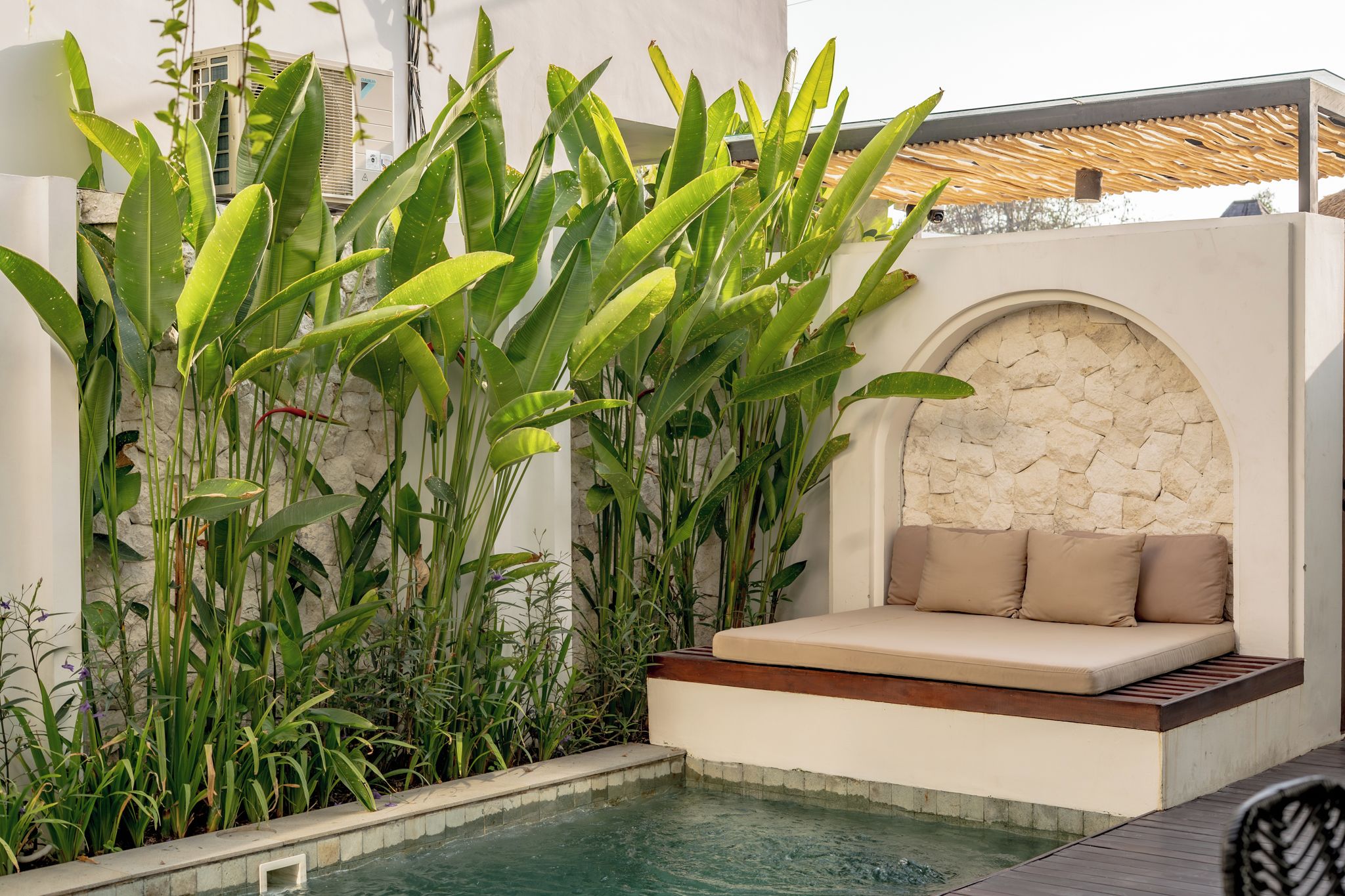 A poolside seating area with a stone wall backdrop and lush tropical plants.
