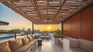 Een dakterras met een houten pergola, een zithoek en uitzicht op de zonsondergang.