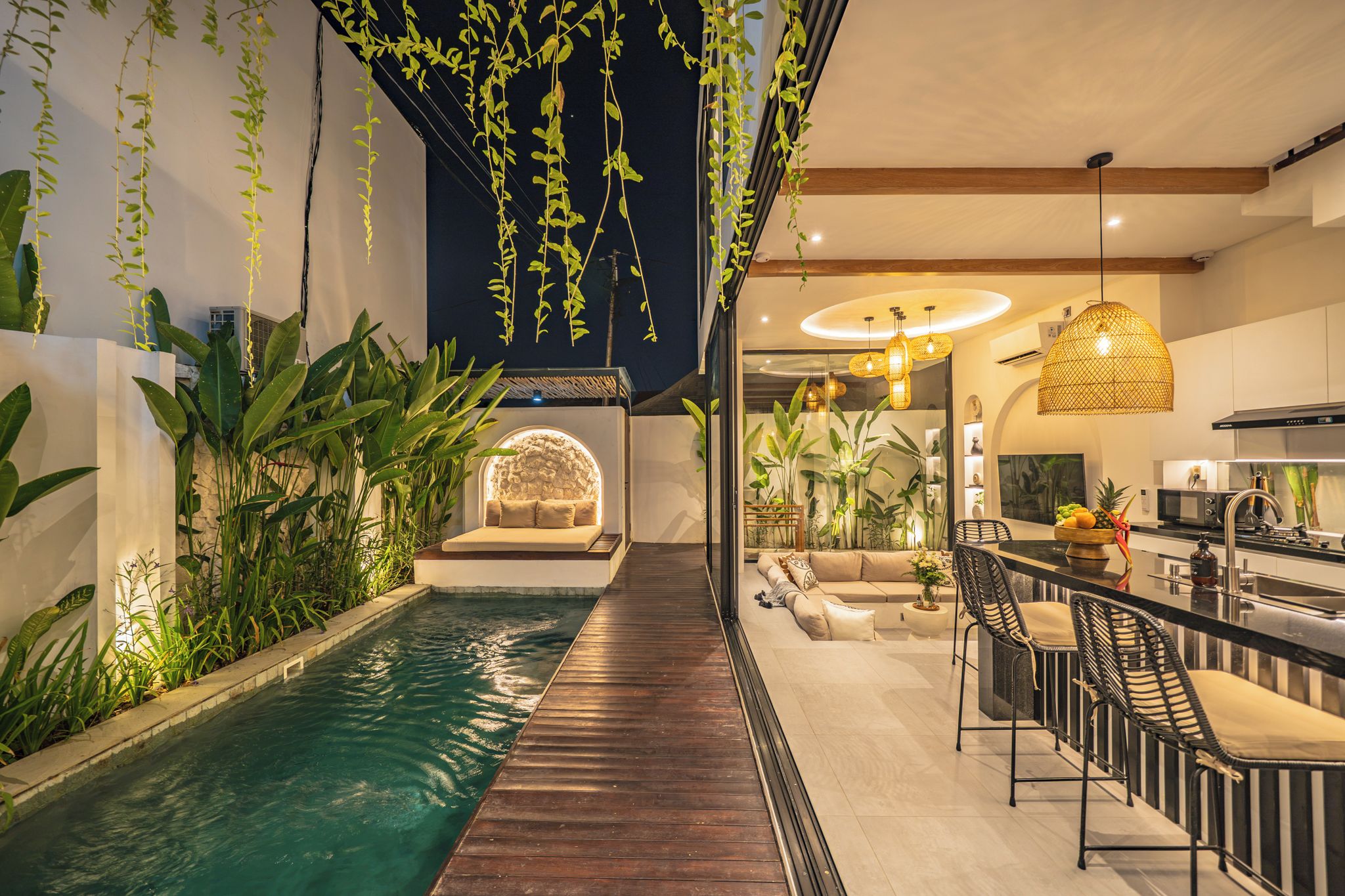 A modern indoor pool area with a wooden deck, seating, and lush greenery.