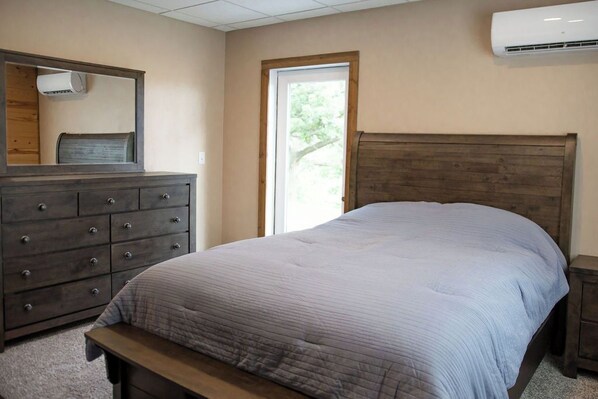 A bedroom with a bed, a dresser, a bench, a window, and an air conditioning unit.