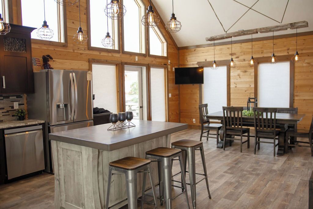 A modern kitchen with a large island, bar stools, wooden flooring, and a dining area with a table and chairs.