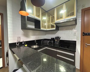 Eine Küche mit einer Granit-Arbeitsplatte, einem Edelstahl-Spülbecken, schwarzen Schränken und einer schwarzen Dunstabzugshaube.