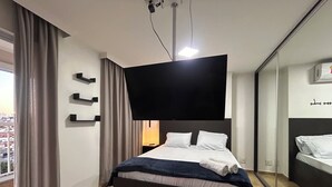 Una camera d'hotel moderna con un ampio letto, una TV a schermo piatto montata a parete, un comodino e un grande specchio.