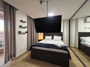 Ein modernes Hotelzimmer mit einem großen Bett, einem flachbildfernseher an der Wand, einem Nachttisch und einem großen Spiegel.