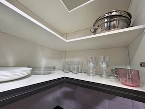 A kitchen with white cabinets, a black countertop, and a stainless steel colander on the shelf. - Apto 1111- Próx Aeroporto de Guarulhos (Guarulhos)