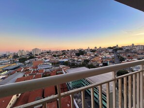 A cityscape with a mix of residential and commercial buildings, a clear sky, and a balcony railing. - Apto 1111- Próx Aeroporto de Guarulhos (Guarulhos)