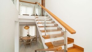A modern staircase with glass railings and wooden steps, leading to a dining area with a round table and chairs. - Luxury 4BR Villa with Private Pool • 5 Min to Playa Dorada (Puerto Plata)