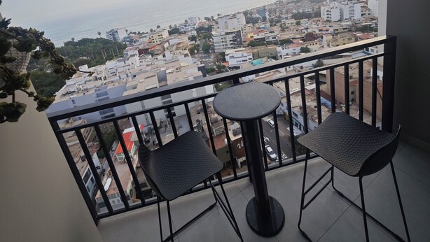 Ein Balkon mit zwei Stühlen und einem kleinen Tisch, mit Blick auf eine Stadtlandschaft mit Gebäuden und einem Gewässer.