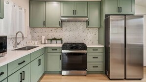 A kitchen with green cabinets, a stainless steel stove, and a double-door refrigerator. - Sunny Nest |Cowboy Pool & Bacyard| Newly Renovated (La Puente)