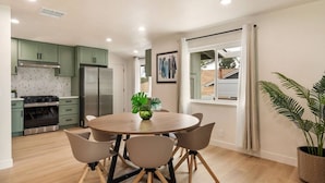 A modern kitchen with green cabinets, a round dining table with chairs, and a potted plant. - Sunny Nest |Cowboy Pool & Bacyard| Newly Renovated (La Puente)