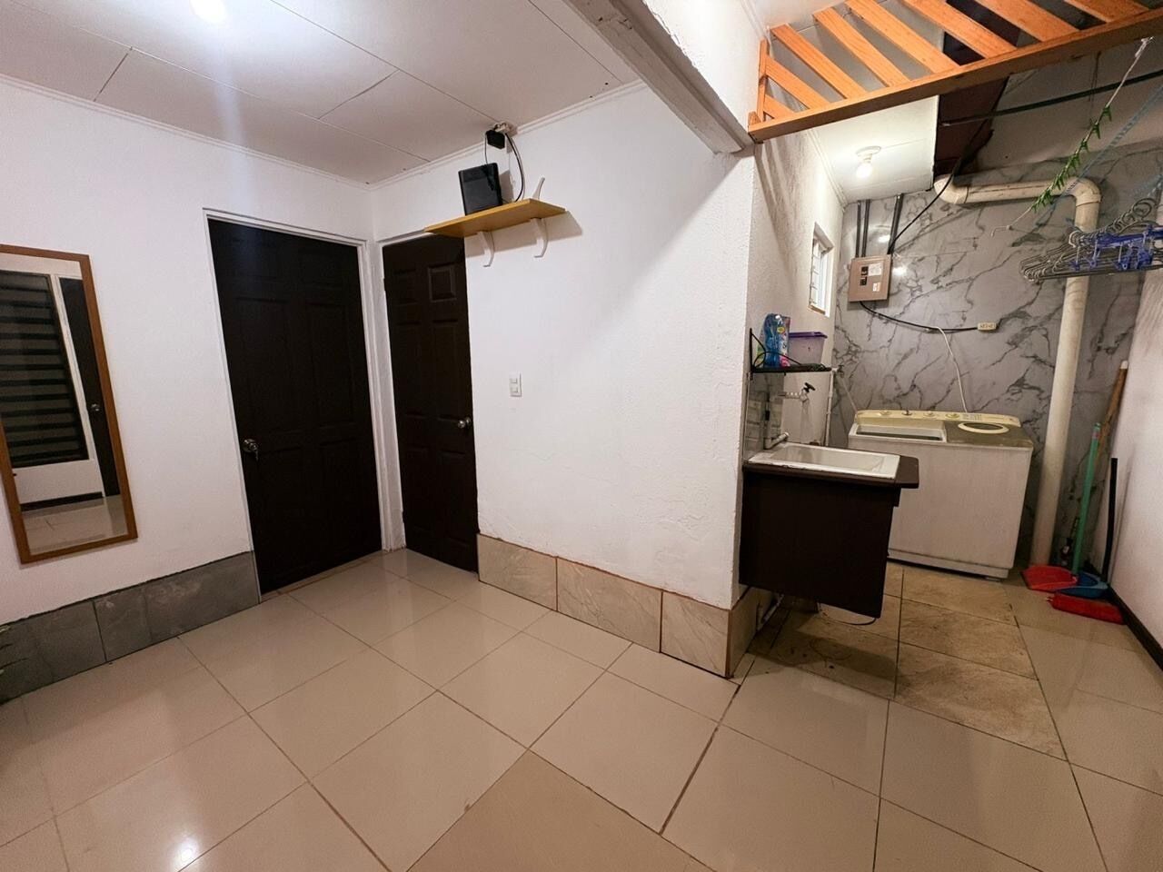 Une pièce avec un sol carrelé, un lavabo, un miroir et une porte.