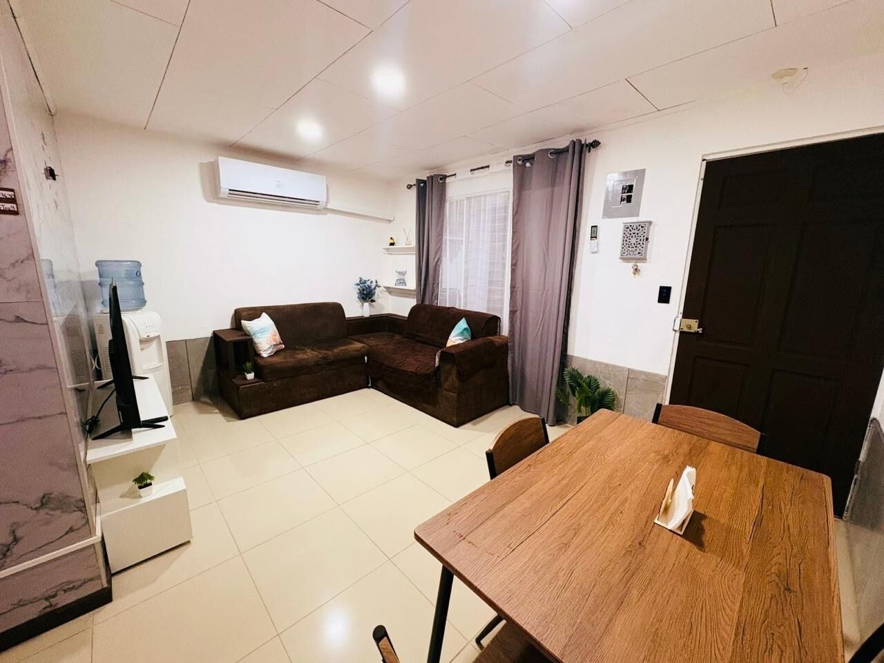 A living room with a brown sofa set, a wooden dining table, and a TV on a stand.
