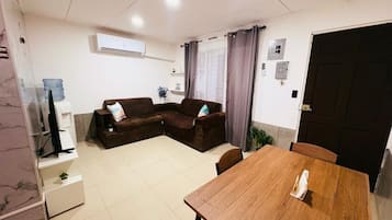 A living room with a brown sofa set, a wooden dining table, and a TV on a stand.