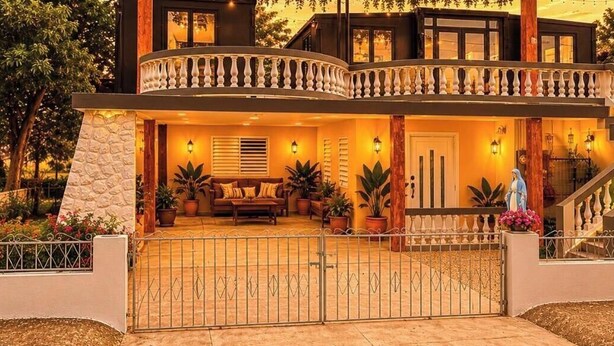 Una casa a più piani con un balcone, una scala e un ingresso chiuso da cancello.