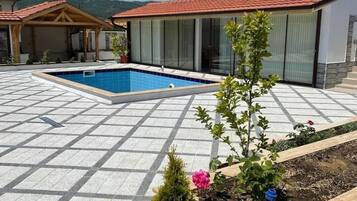 Une piscine avec une terrasse carrelée, un bâtiment doté de grandes fenêtres et un paysage montagneux en arrière-plan.