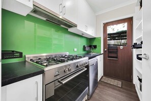 Eine Küche mit Gasherd, Backofen und Geschirrspüler, einer grünen Spritzschutzwand, weißen Schränken und einer Holztür.