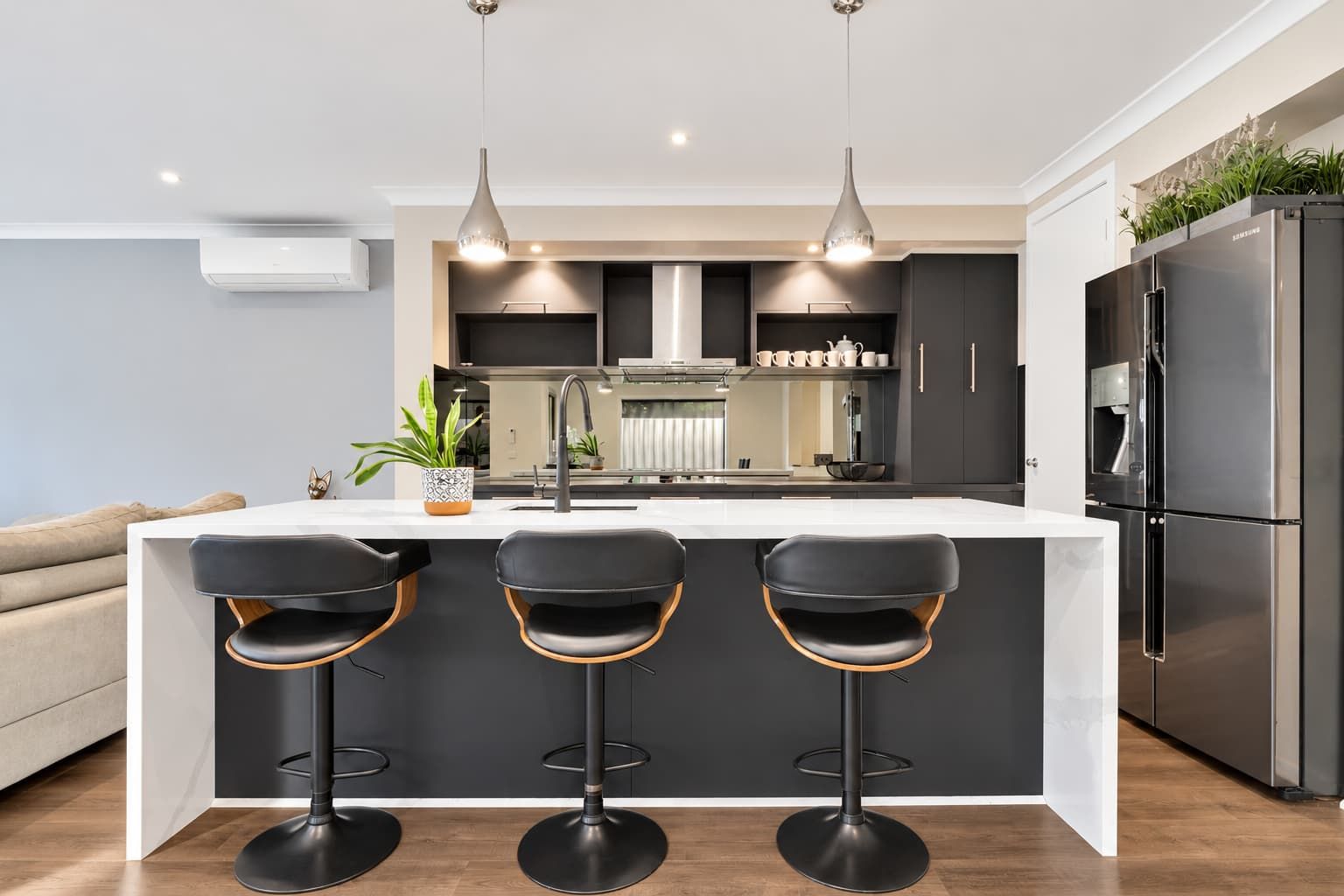 A modern kitchen with a central island, bar stools, stainless steel appliances, pendant lighting, and a built-in oven.