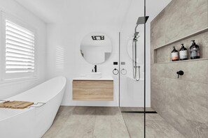 Ein modernes Badezimmer mit einer Badewanne, einem runden Spiegel, einer Dusche und einem Ablagebereich für Pflegeprodukte.