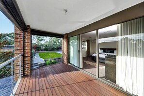 Ein Balkon mit Holzboden, einer Backsteinmauer und einer Glastür zu einem Zimmer mit Bett und Schlafsofa.