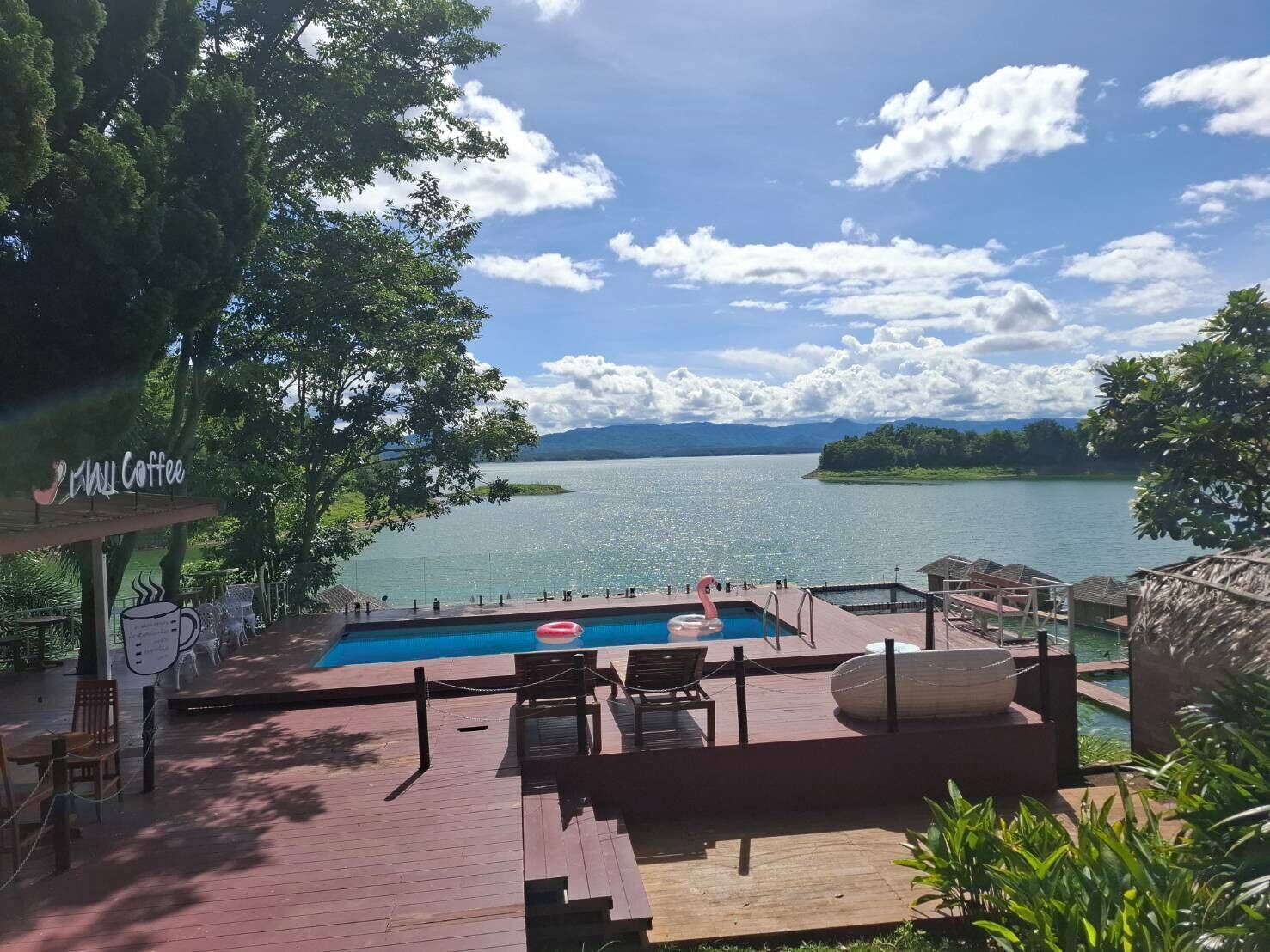 A pool area with lounge chairs, a flamingo decoration, and a view of a lake and mountains.