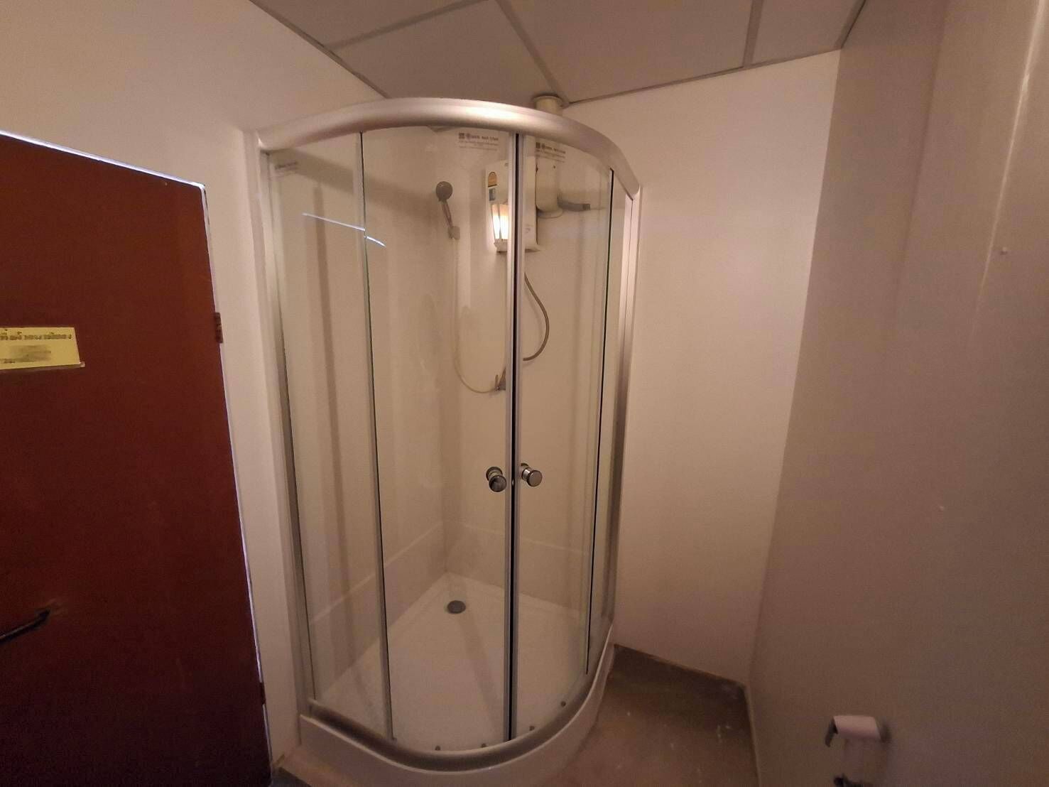 Un vestuario de ducha con paredes de vidrio, una puerta, un perchero y un secador de manos.