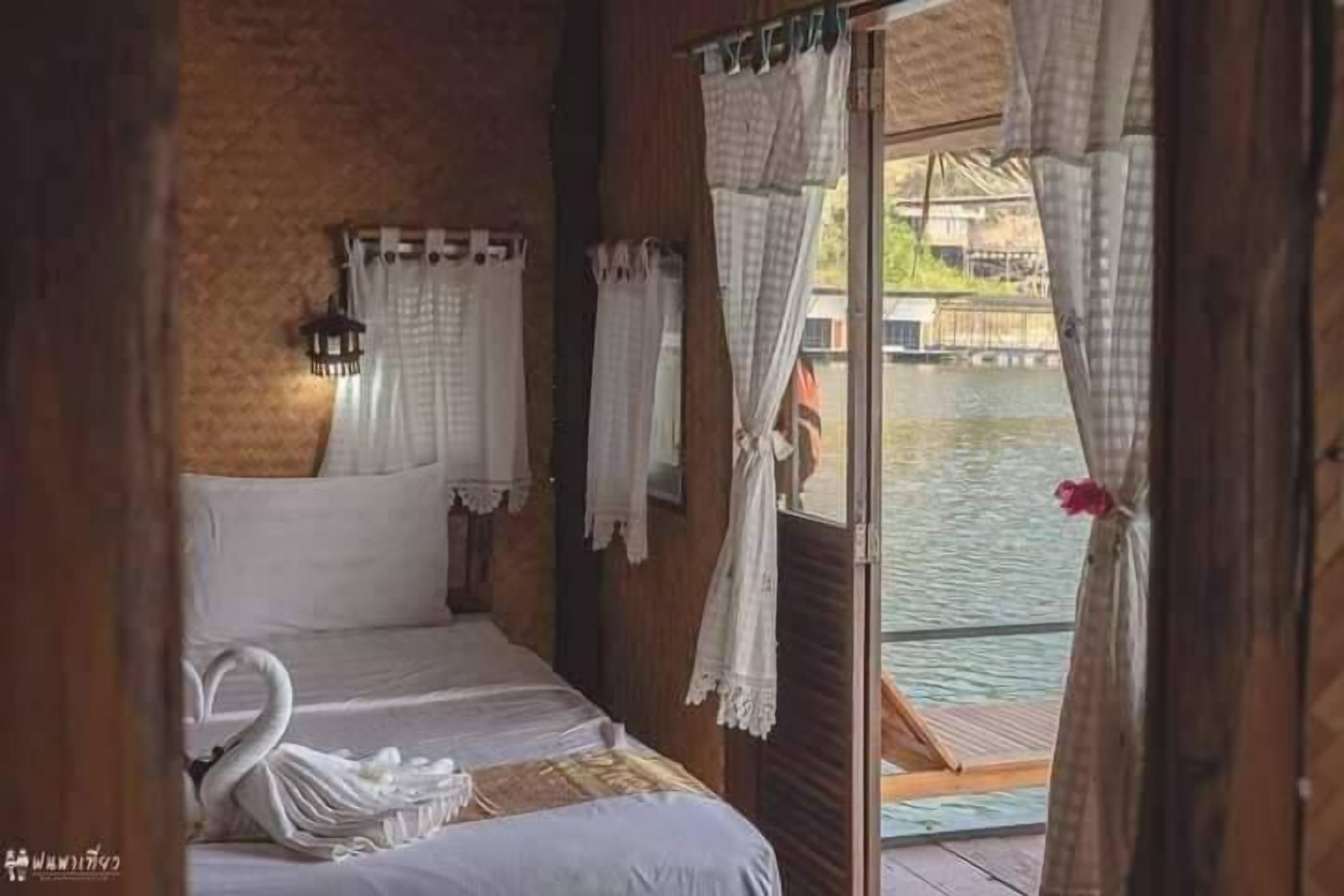 Quarto de cabana de madeira com cama, cortinas e vista para um corpo de água.