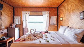 Habitación de hotel con una cama grande, un escritorio, un refrigerador y vista al agua.