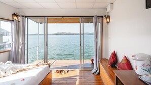 A room with a bed, a wooden bench, a table with a kettle, and a view of the water.