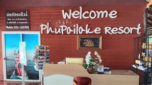 A reception area at Phu Poiloke Resort with a welcome sign, a framed picture, a desk, a chair, and a poster of a boat.