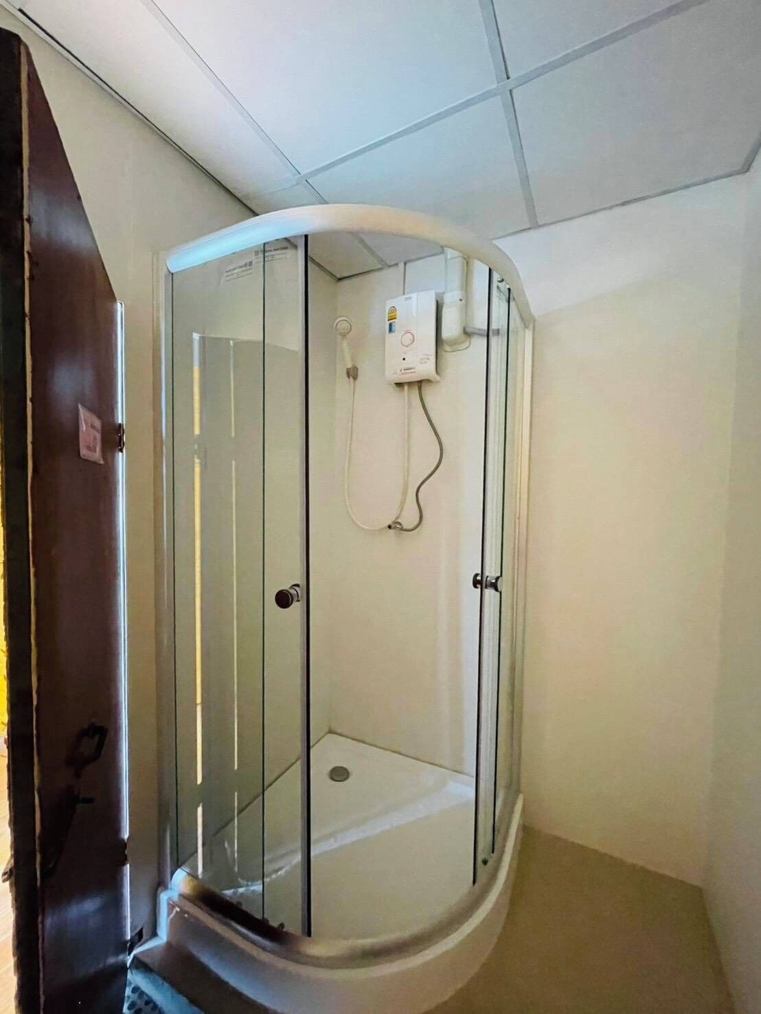 A corner shower room with a glass enclosure, a control panel, and a door.