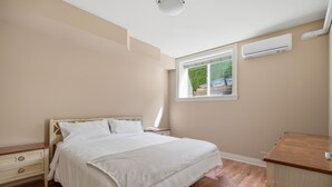 A bedroom with a bed, nightstands, a dresser, and a window with a view of greenery.