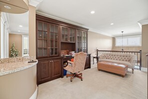A spacious living room with a large dark wooden cabinet, a plush beige sofa, and a rolling office chair.