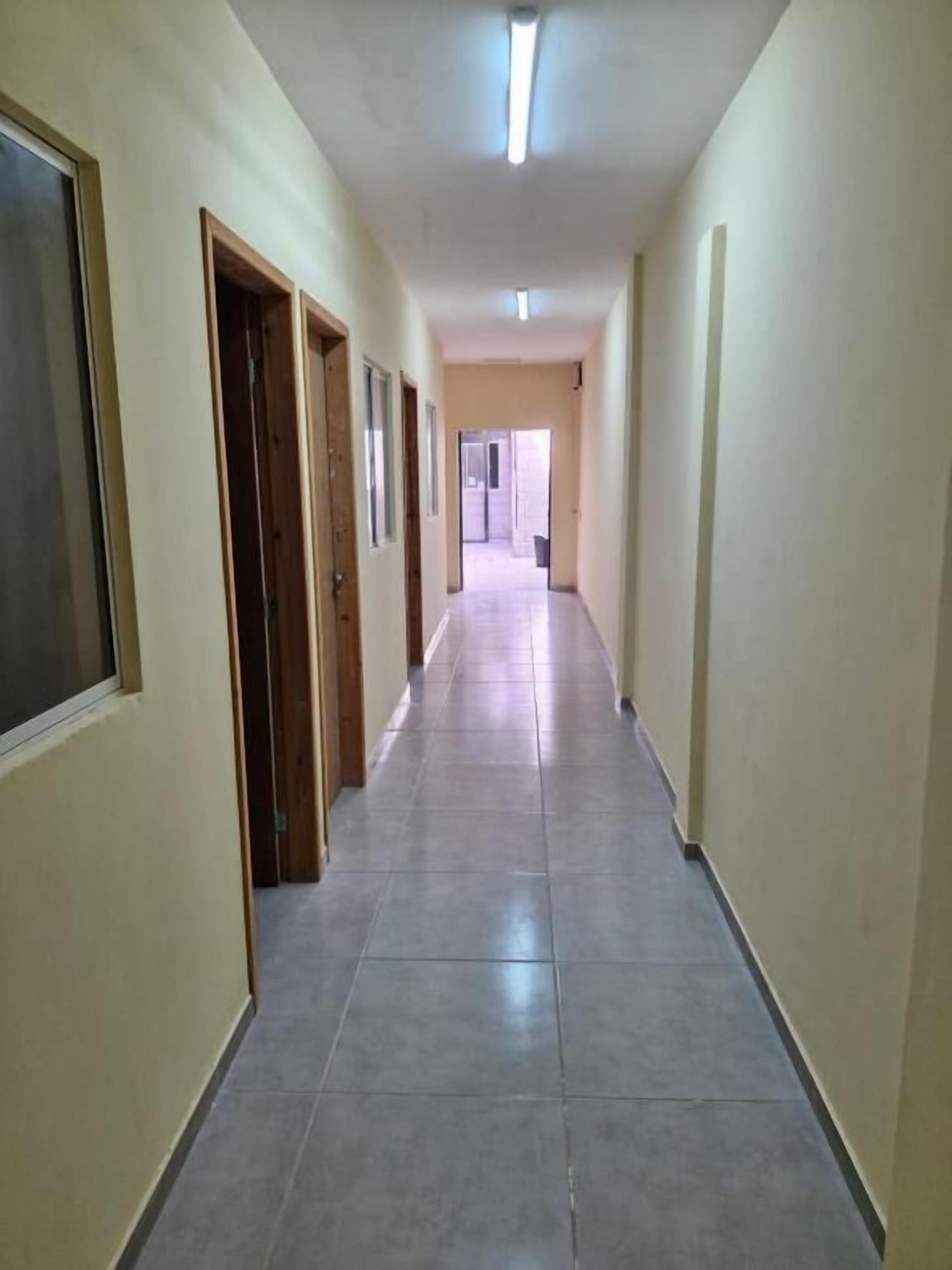A long, narrow hallway with doors on one side and a plain wall on the other.
