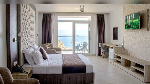 A hotel room with a bed, a desk, a TV, and a view of the sea. - Hotel Cap Carbon (Béjaïa)
