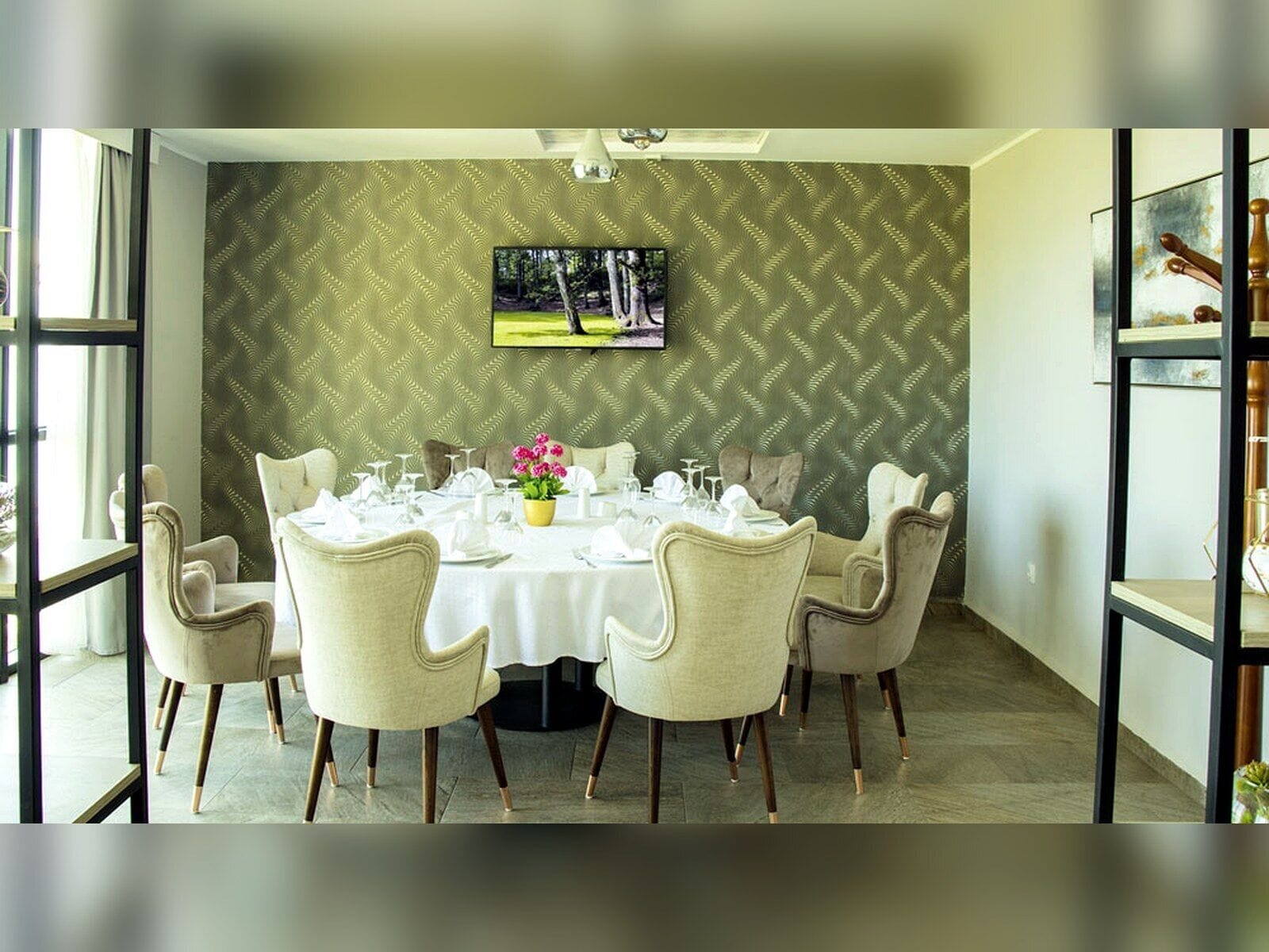 A dining area with a round table set for six, surrounded by six chairs. A television is mounted on the wall above the table.