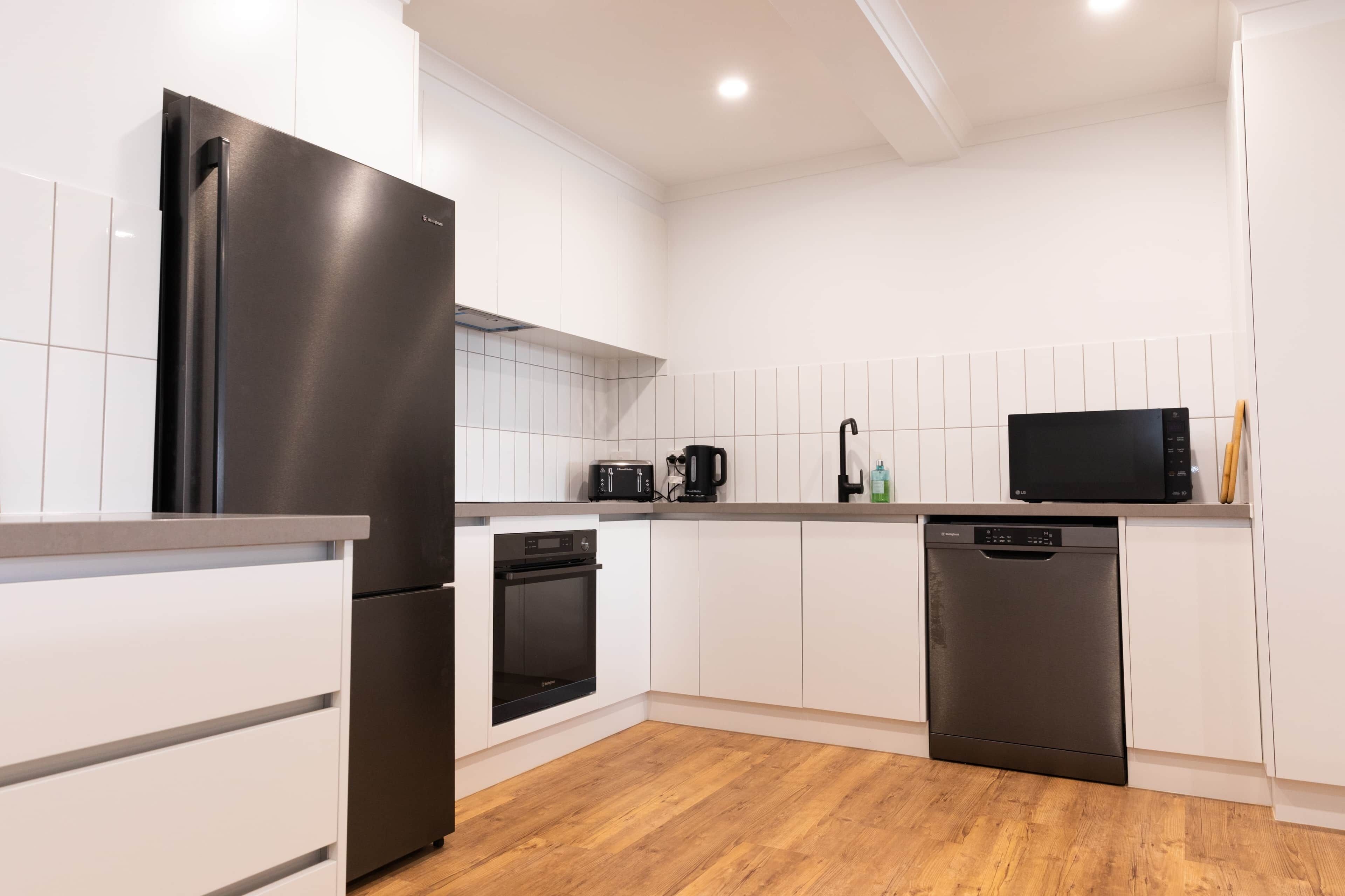 Una cocina moderna con armarios blancos, un refrigerador de acero inoxidable, un horno, un lavavajillas y un microondas.