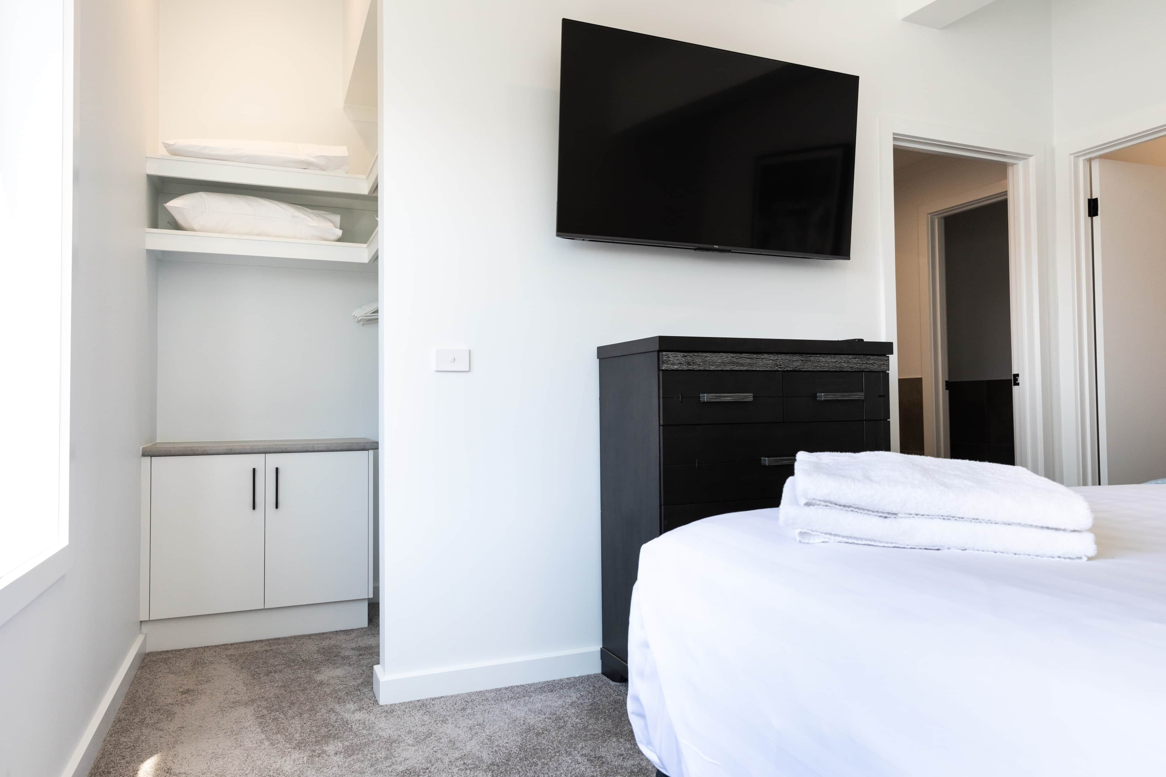 Une chambre d’hôtel comprenant un lit, un téléviseur fixé au mur, une armoire et un placard avec des étagères.