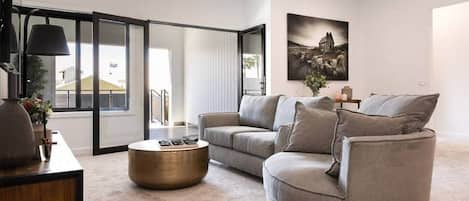 A modern living room with a grey sofa, a round coffee table, and a large window with a view of buildings.