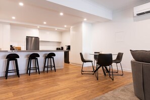 A modern kitchen with a central island, bar stools, a dining table with chairs, and a sofa. - The Lime Loft | Rooftop Views in Mildura's CBD (Mildura)