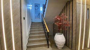 A staircase with a wooden finish, a white vase with red foliage, and a wall with vertical lines. - LinQues Residences (Ibadan)