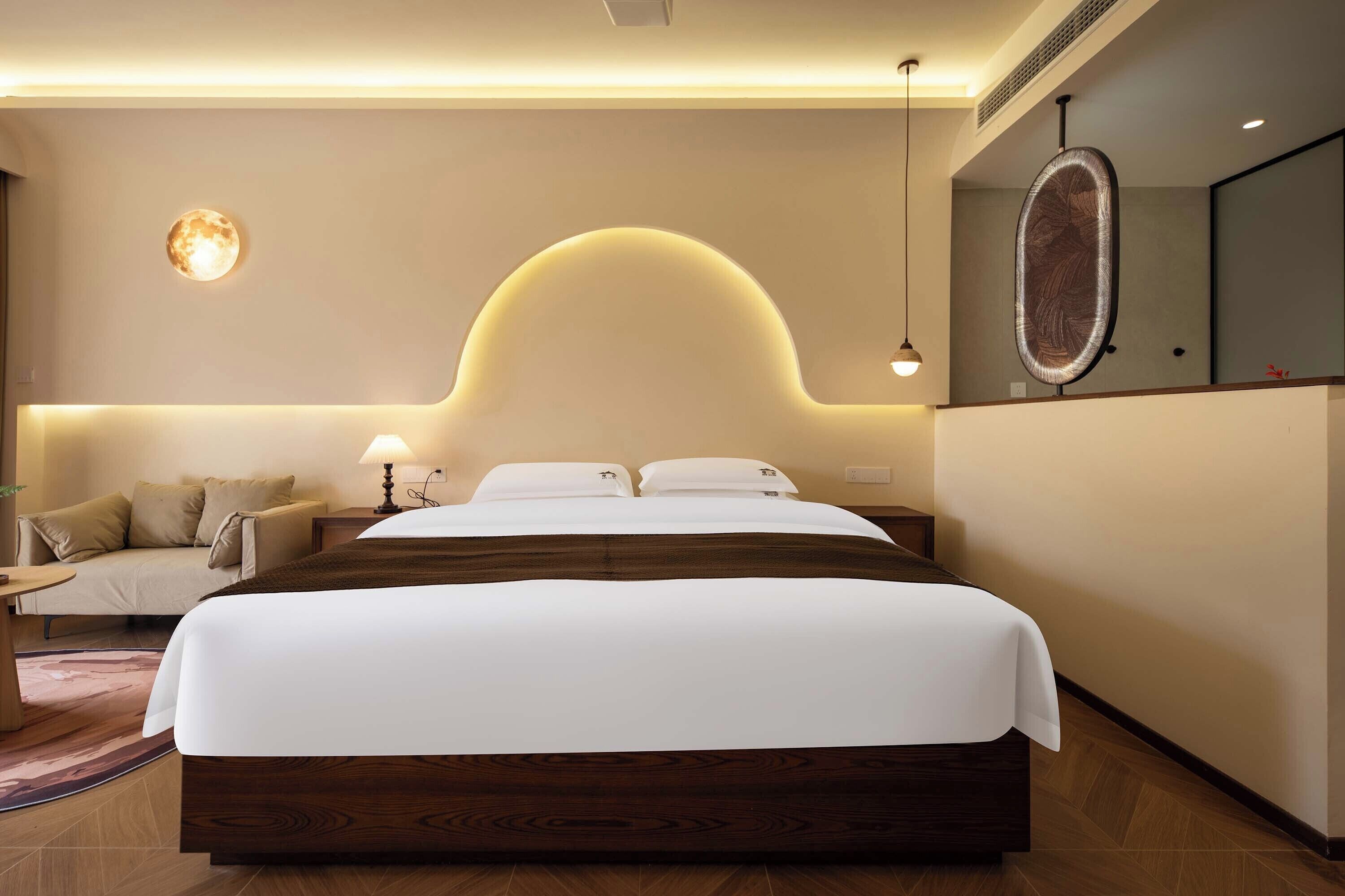 Ein modernes Hotelzimmer mit einem großen Bett, einer Couch, einem Schreibtisch und einem Wandspiegel.