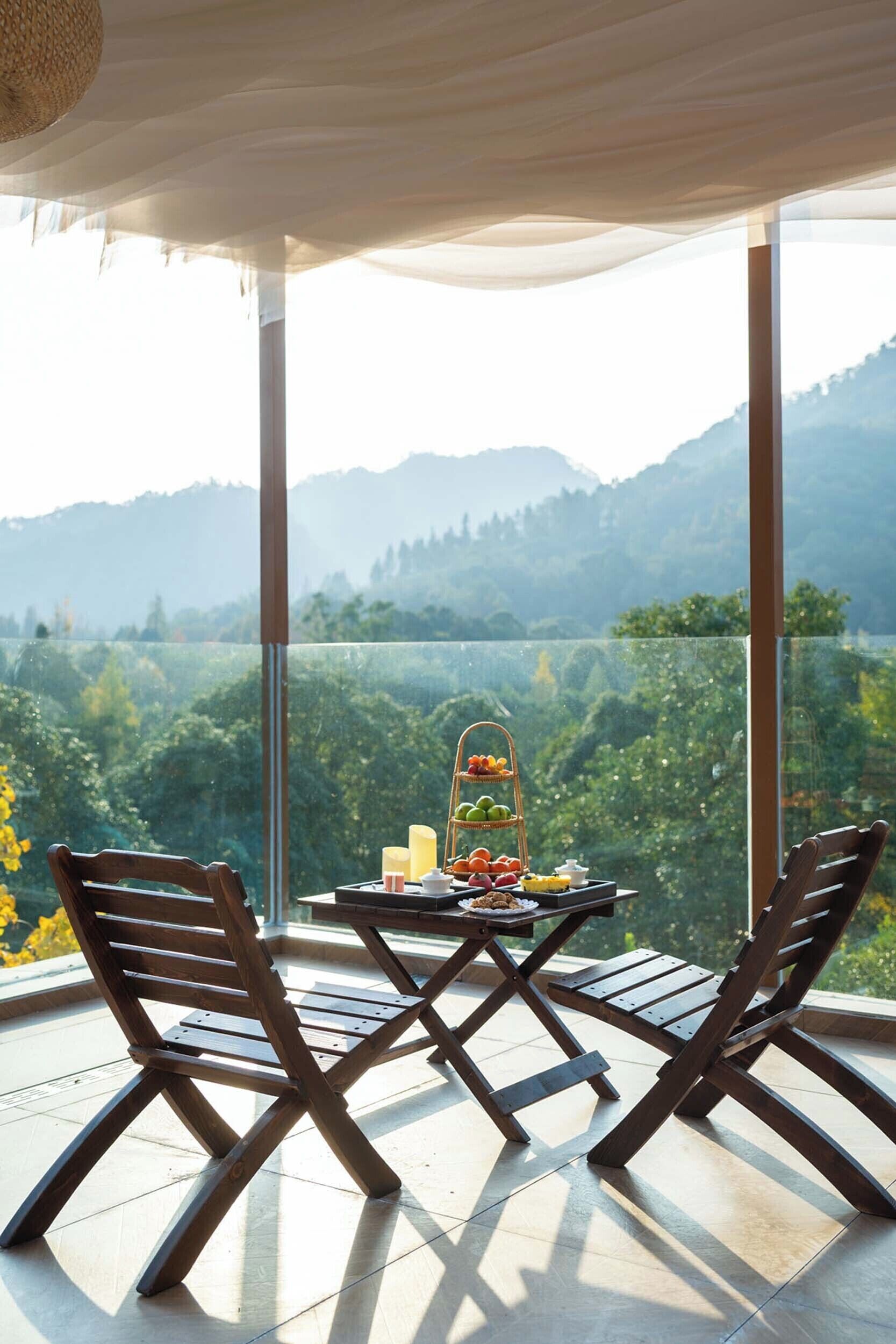 A balcony with a table set for two, overlooking a mountainous landscape.