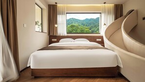 Un dormitorio con una cama grande, vistas a un bosque y una pared curva.